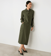 Full body view of a model wearing the Alexa Khaki Utility Jacket buttoned up facing side-on, leaning against the wall.