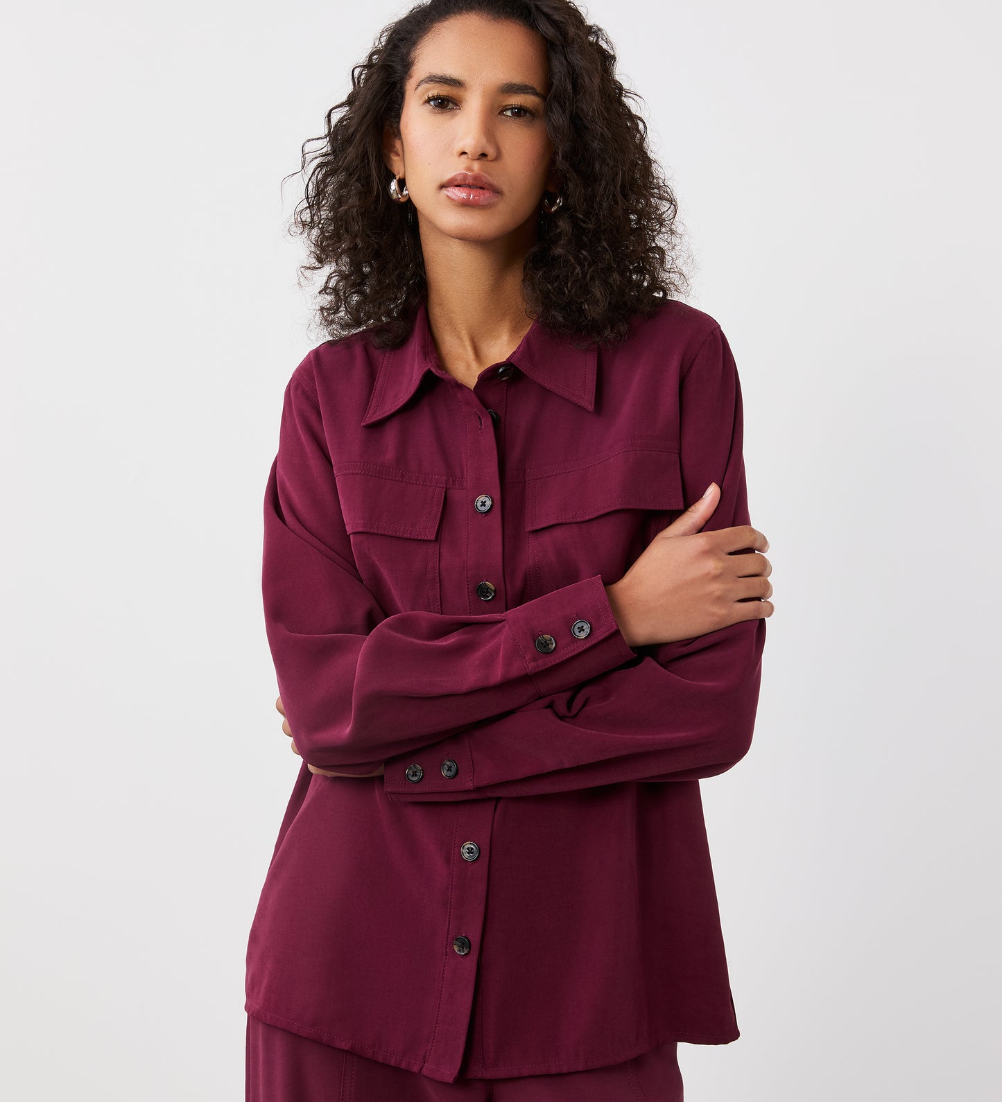 Close-up view of a model wearing the Nicola Merlot Utility Shirt facing forward, arms crossed.